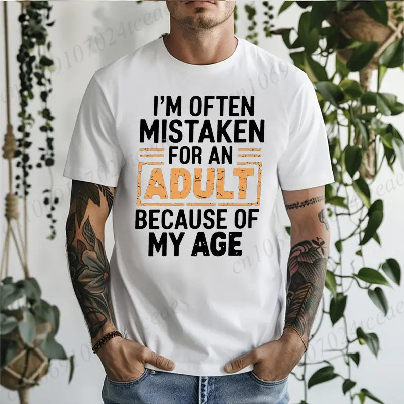 Camiseta de algodón blanca con texto desgastado negro y naranja que dice: «A menudo me confunden con un adulto debido a mi edad», diseñada como una camiseta con gráfico humorístico de adulto de broma para mayores.