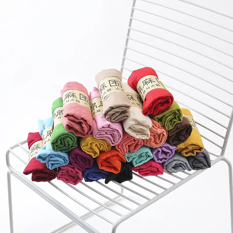 A colorful assortment of rolled-up cotton winter scarves for women in various solid hues each wrapped with a beige paper label bearing Chinese characters.