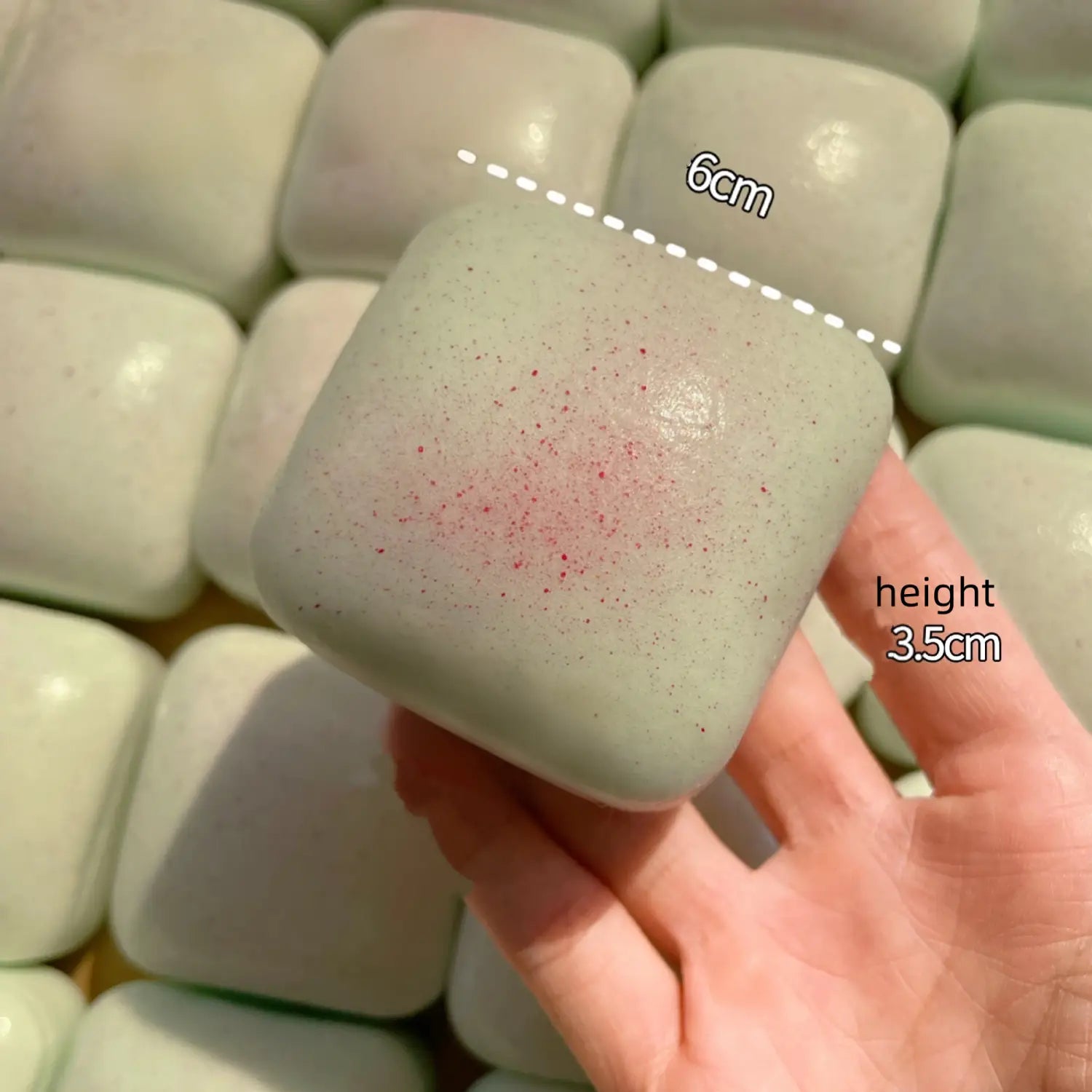 mini toast carré, vert pâle, à dégagement lent, jouet sensoriel d’agitation, avec une texture légèrement mouchetée et de légers éclats rouges, présenté de face, selon un angle avant