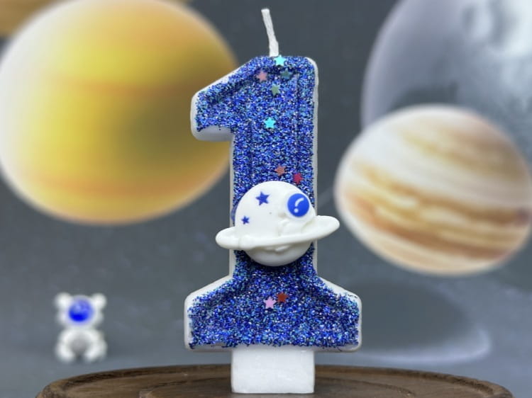 Vela azul con brillo con el número uno para cumpleaños, con una figura de astronauta blanca en su base, utilizada como adorno para pastel de fiesta planetaria de velas de cumpleaños numerales del espacio.