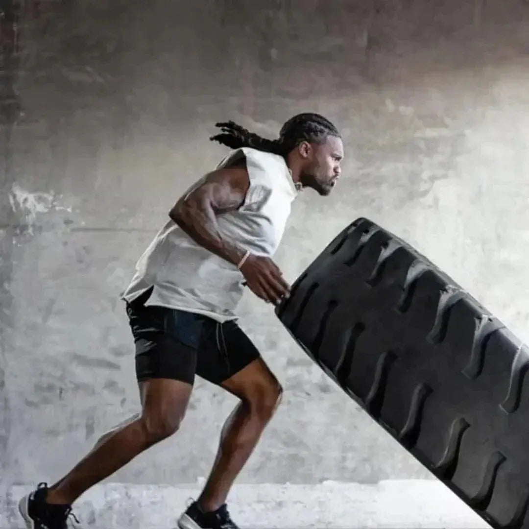 Neumático de caucho negro con banda de rodadura profunda y diseño resistente, mostrado junto con pantalones cortos de entrenamiento para anime de gimnasio 2 en 1 para hombres con trabilla para la toalla que ofrece soporte.