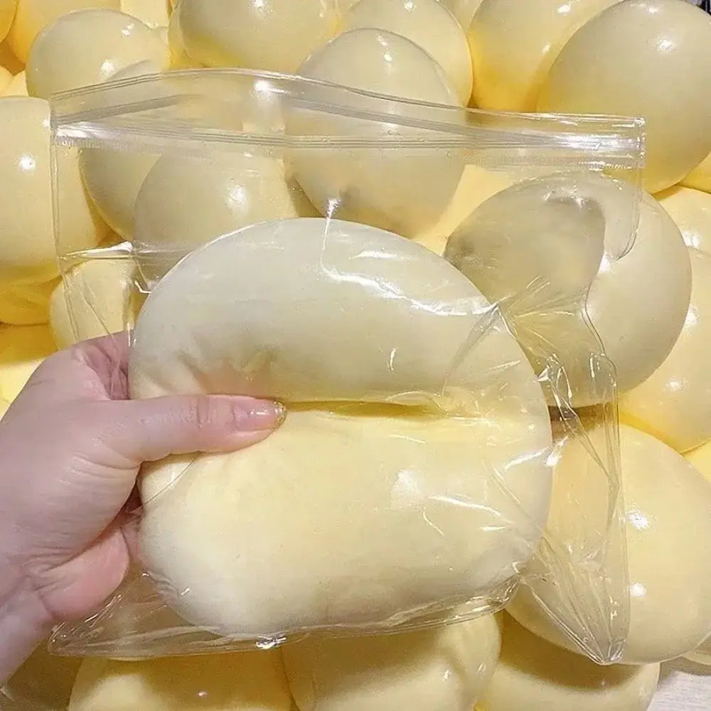Una pelota blanda y esponjosa de silicona color amarillo pálido, con forma de dona, para aliviar el estrés, envuelta en una bolsa de plástico transparente.