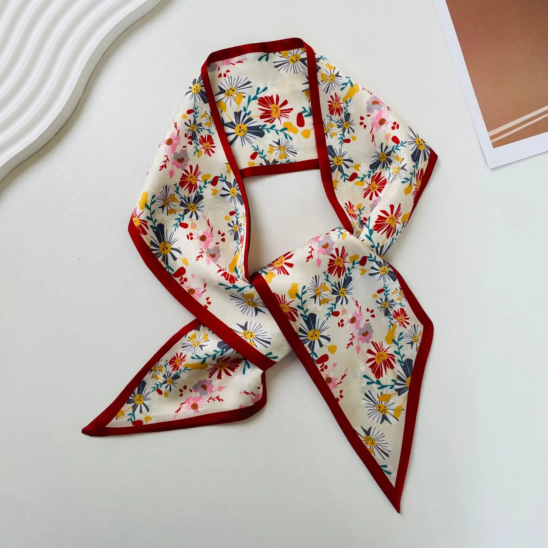 Pañuelo de seda con estampado geométrico, con escote cuadrado, que presenta una tela de seda con estampado floral vibrante sobre base crema, con flores en rojo, amarillo, rosa y azul enmarcadas por un borde carmesí sólido.
