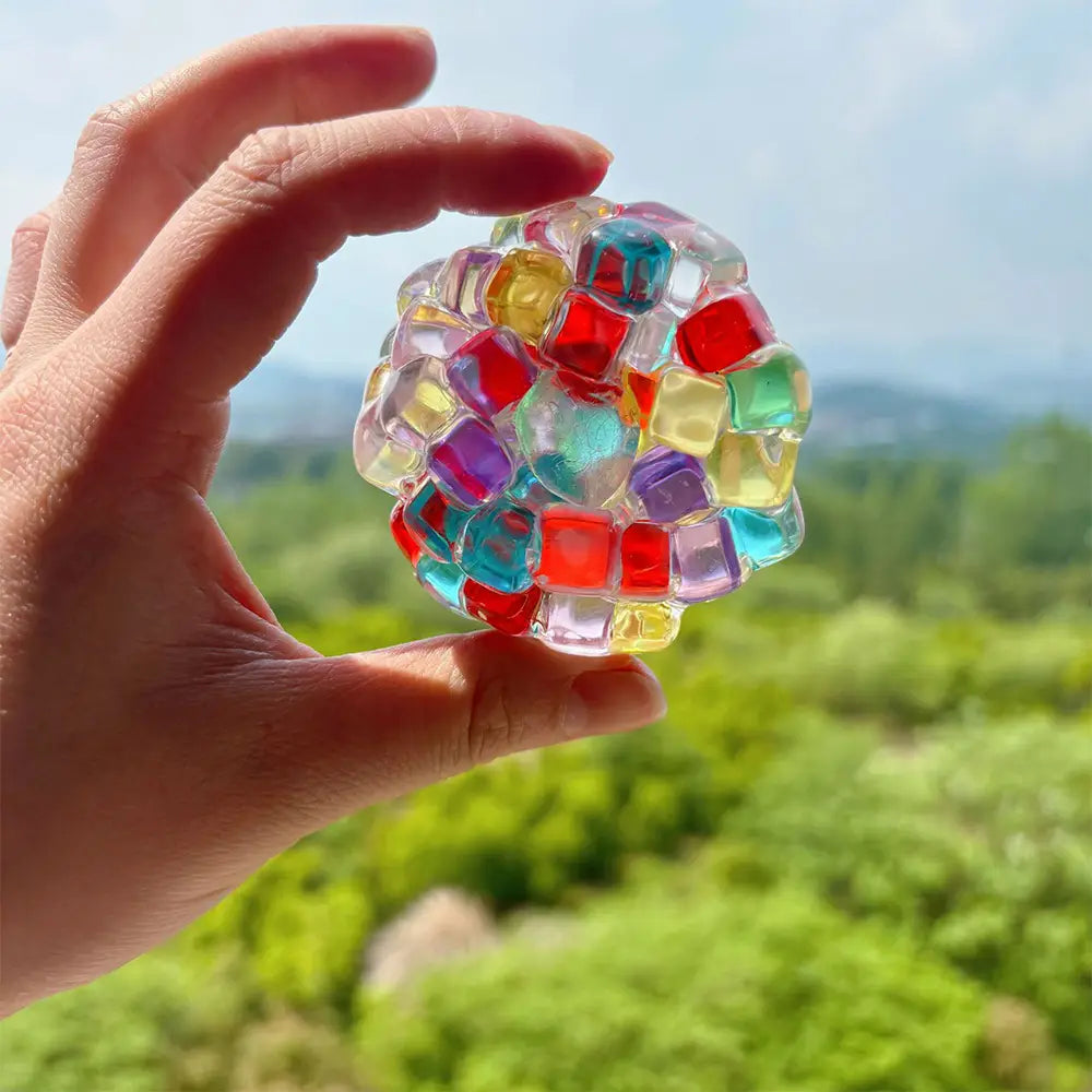 Jouet anti-stress à perles de glace en gel à presser, en gel translucide coloré, façonné comme une balle d’occupation, avec des segments carrés imbriqués dans des tons vifs de rouges, bleus, jaunes et violets.