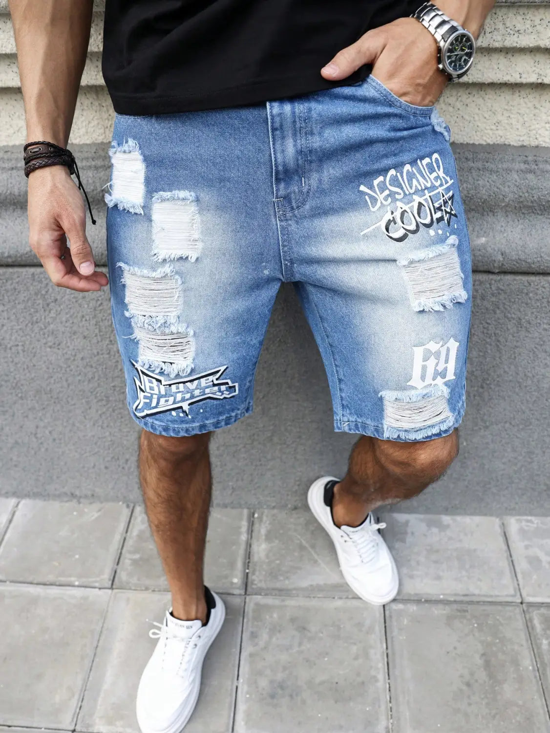 Shorts en jean déchirés pour hommes, de couleur bleue, présentant des patchs abîmés et une impression graffiti blanche, pour une tenue d’été