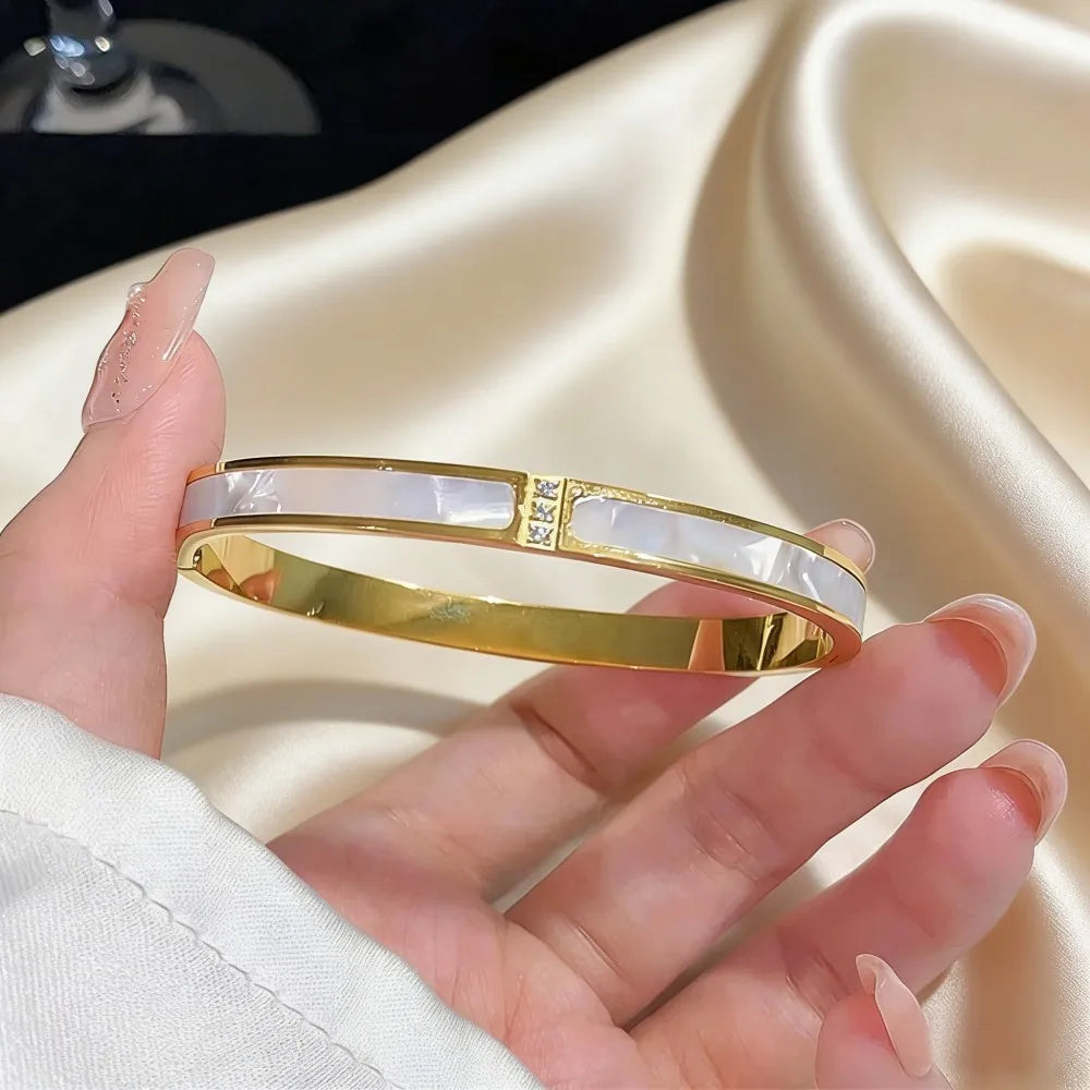Stainless steel gold-toned bangle bracelet for women featuring a central rectangular panel of white mother-of-pearl with embedded clear crystals.