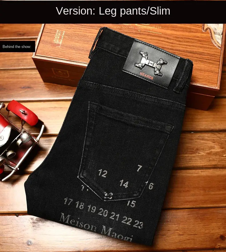 Mens slim fit printed black denim jeans showing the back side with a black leather patch embossed with an h-shaped logo and Hermes text at the waistband.