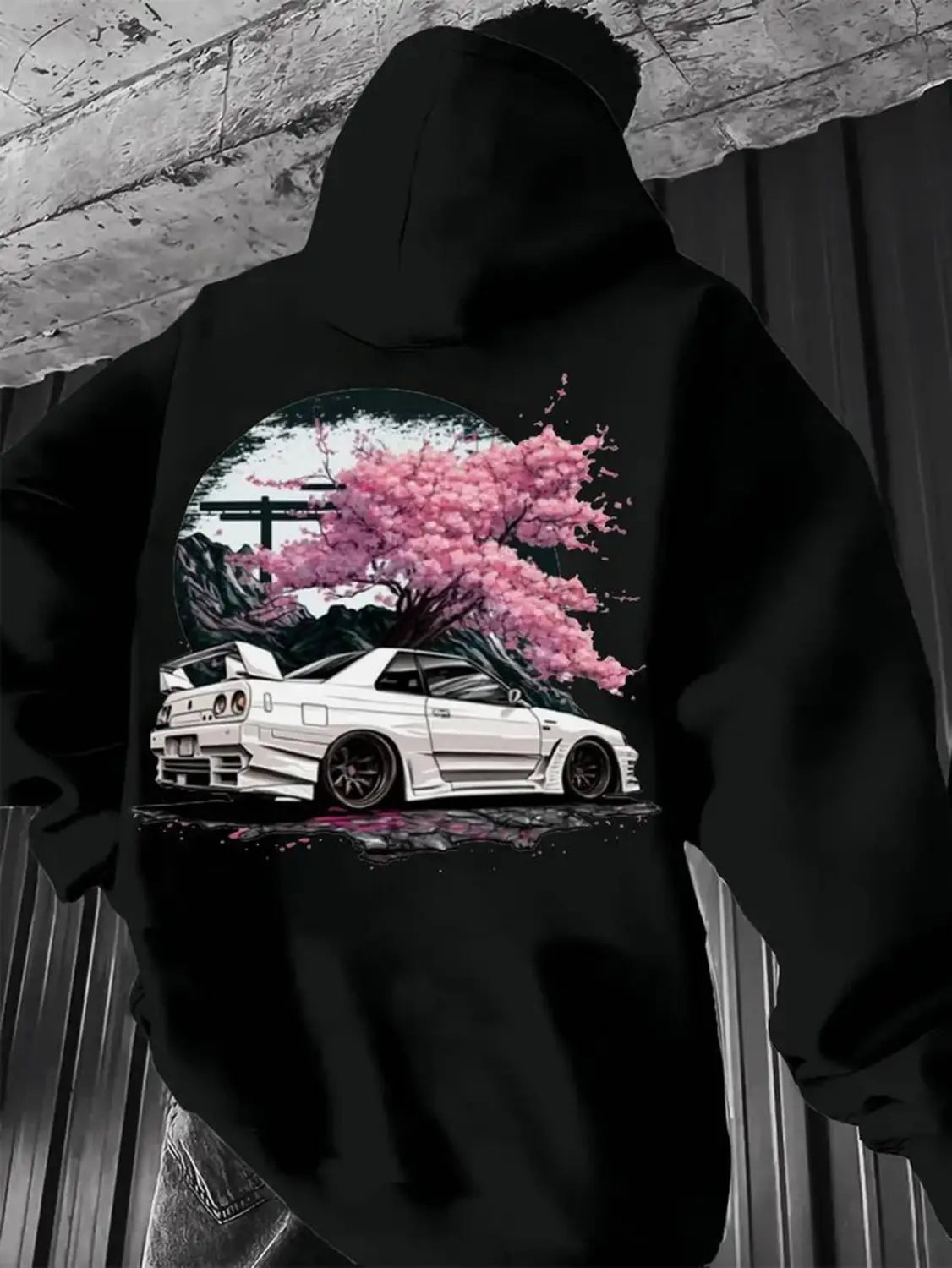 black hoodie featuring a vibrant graphic of a white sports car under a pink cherry blossom tree against a circular backdrop from the jdm skyline cherry blossom men hoodie collection.