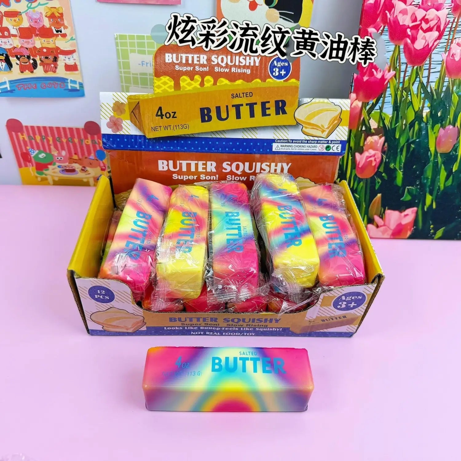 Jouet antistress souple à la forme de beurre à la fraise, en plastique à dégradé arc-en-ciel, à montée lente, avec « beurre » imprimé en lettres bleues épaisses sur sa surface.