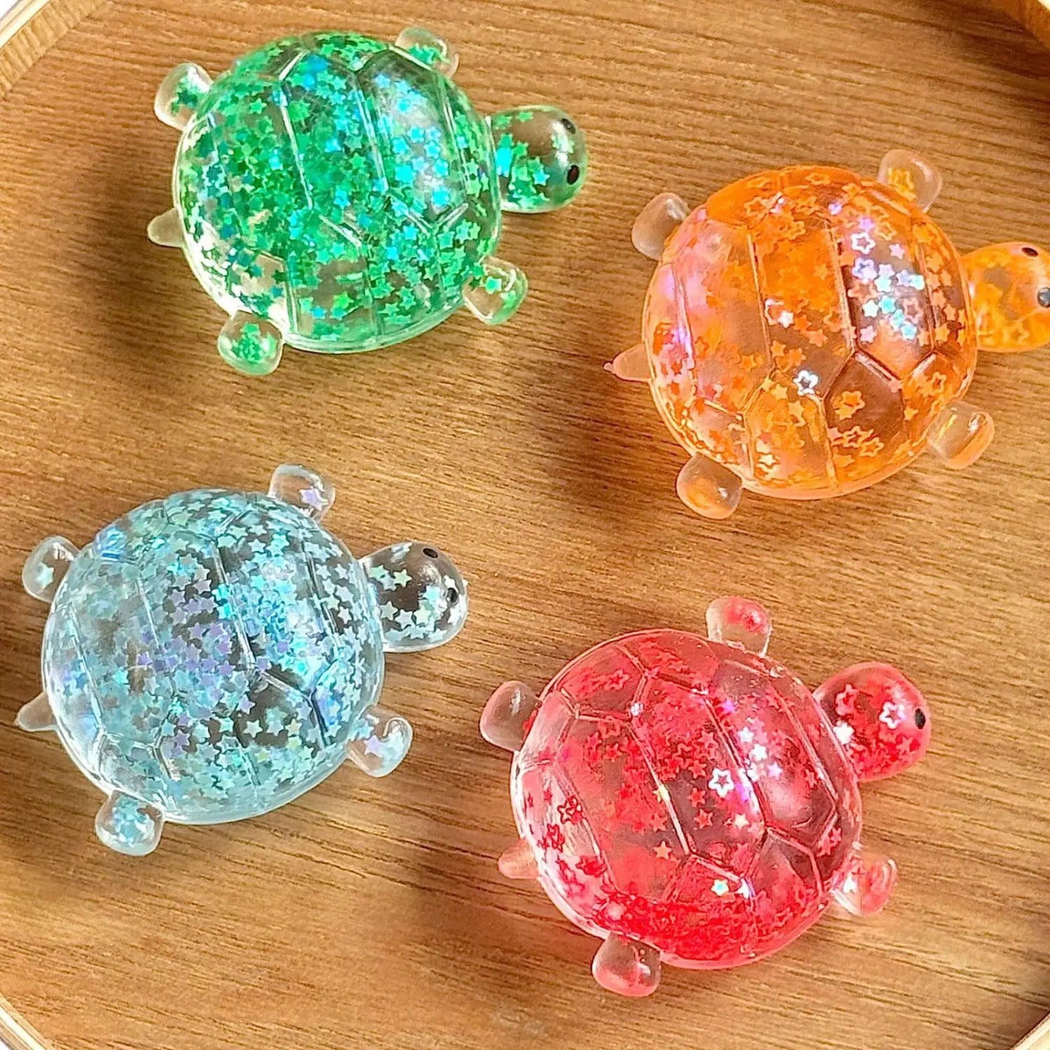 Four colorful translucent turtle shape squeeze toys in green orange blue and red filled with glittering star confetti designed as glitter turtle squeeze toy sensory fidgets.
