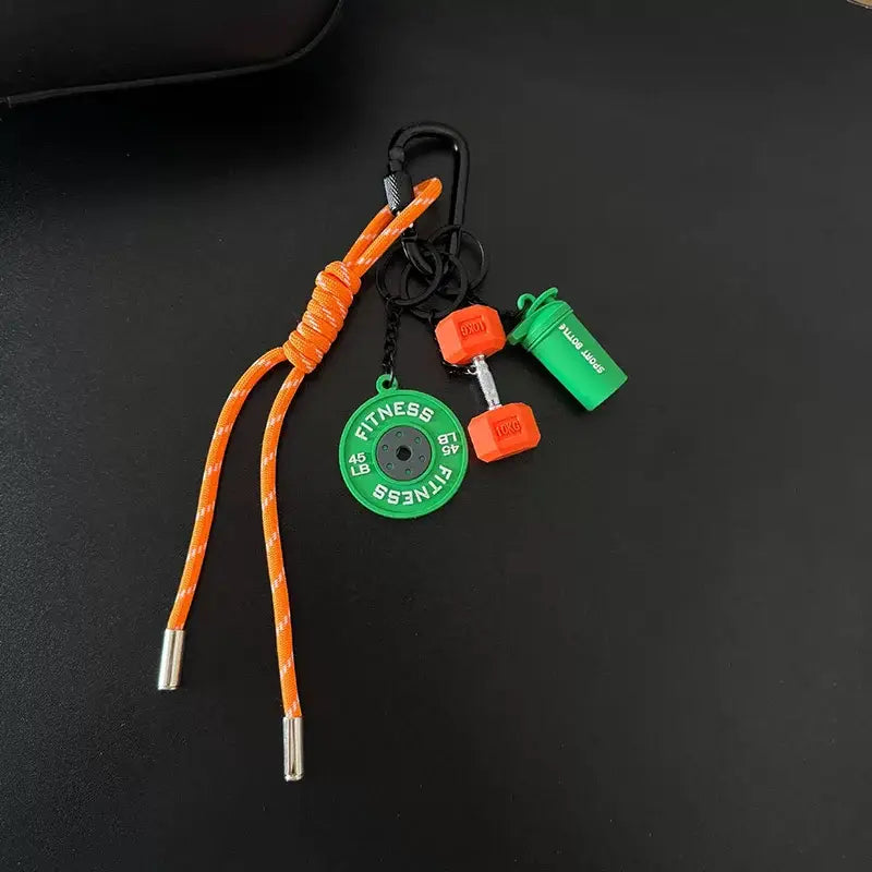 Porte-clés de musculation orange et vert avec cordon tressé comprenant une breloque de disque de poids pour mini-haltère et un accessoire de bouteille shaker, en cadeau de motivation pour l’entraînement.