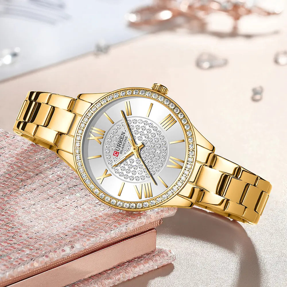 Gold-toned curren women stainless steel crystal quartz watch with a sparkling diamond-studded bezel roman numeral hour markers and a silver dial adorned with embedded crystals.