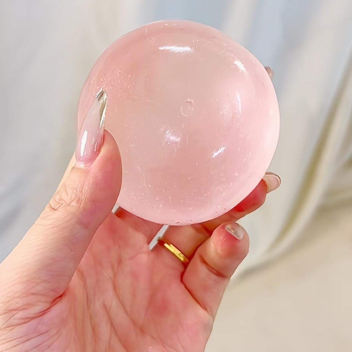 Une balle anti-stress translucide rose de type gel, avec une surface lisse légèrement brillante et des micro-aspérités internes discrètes, conçue comme un jouet de compression « Blue Coconut Oil Stress Ball »