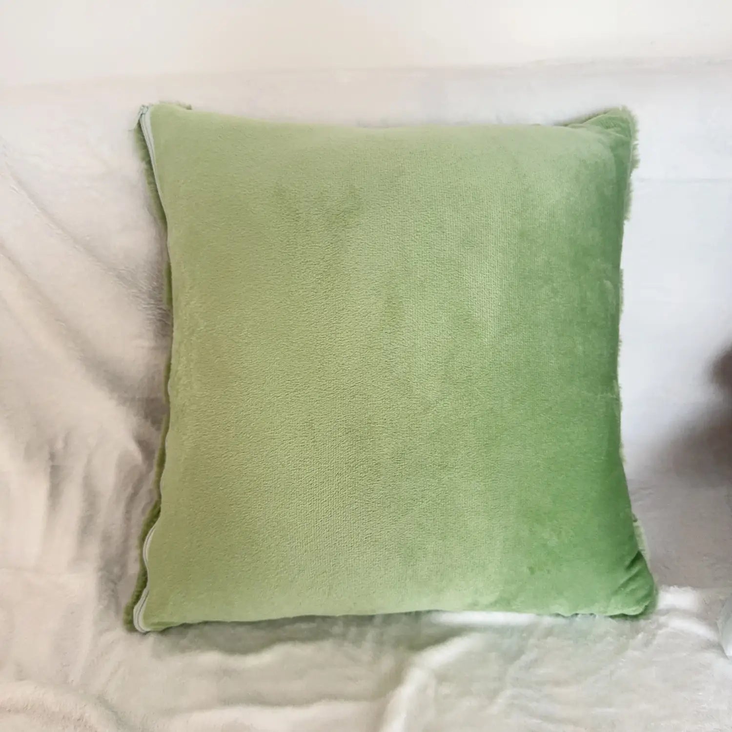 A soft sage green velvet plush leaf embroidered throw pillow cover with a square shape and slightly frayed edge.