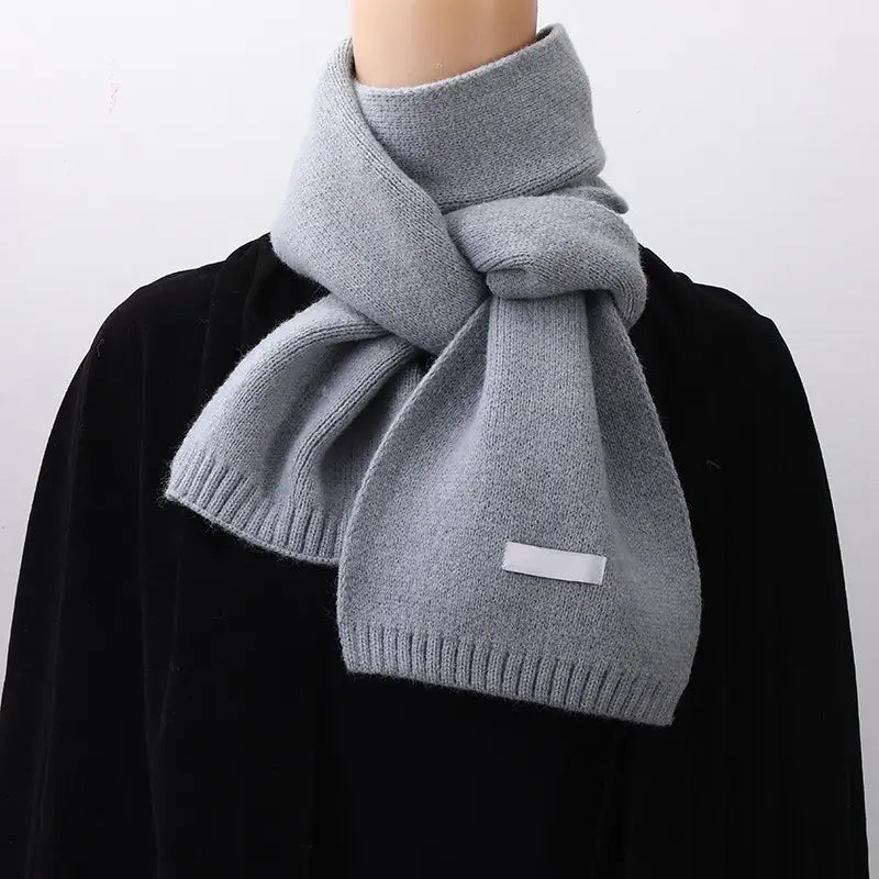 Bufanda de invierno tejida en rojo para hombres y mujeres, en punto gris claro suave, con bordes acanalados y una pequeña etiqueta rectangular blanca.
