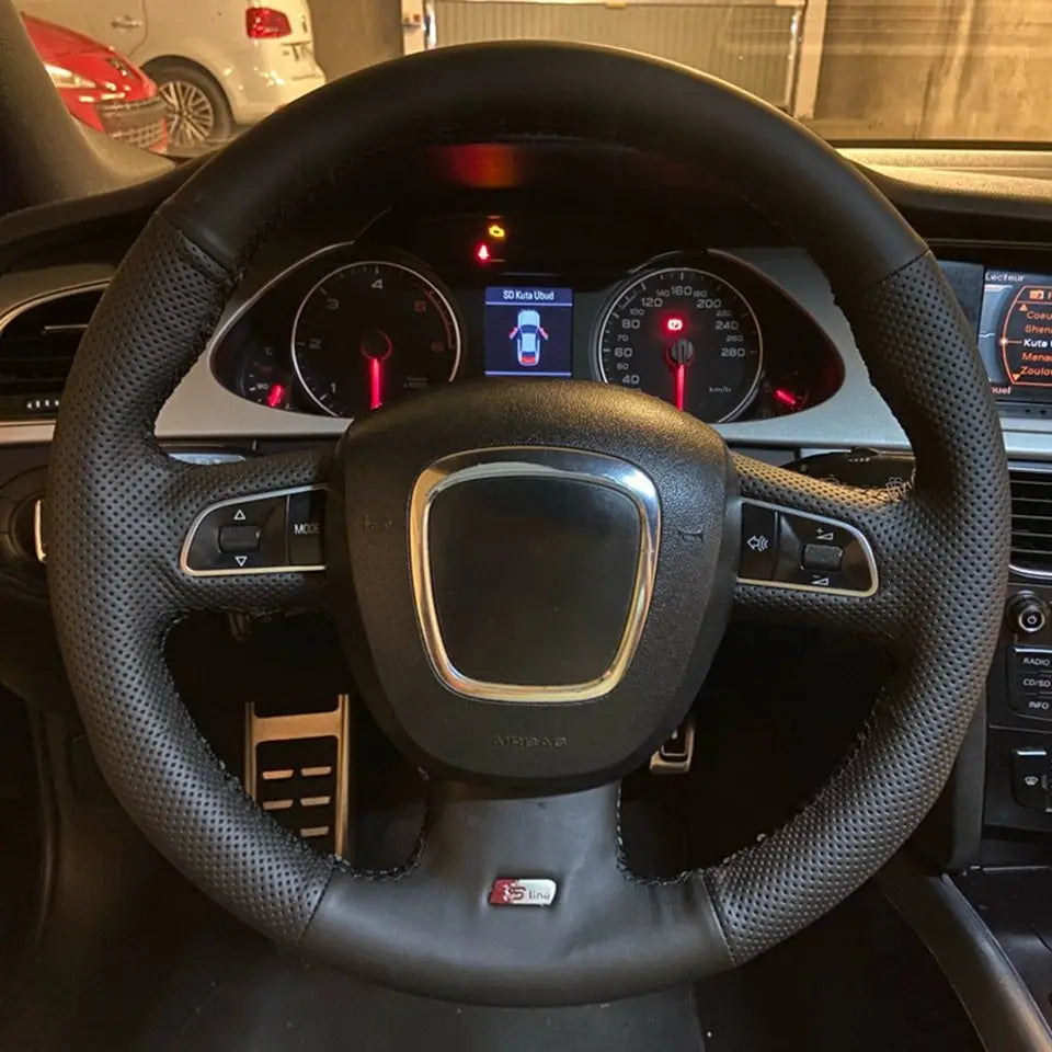 Cubierta para volante de cuero perforado negro de Audi con costuras rojas y centro con acento plateado, que presenta un emblema S line.