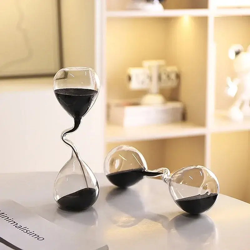 Ein klarer Glas-Stundenglas-Timer mit gedrehter S-förmiger Verjüngung und schwarzem Sand, der zwischen zwei gerundeten Glaskolben fließt, für moderne Wohn-Dekoration und die Verwendung als Sanduhr.
