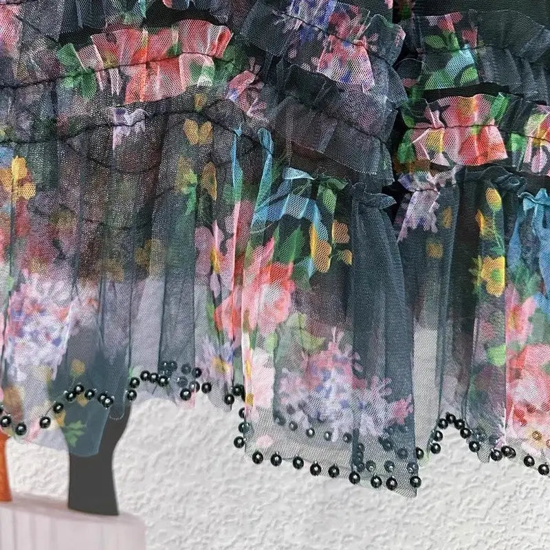 Una falda de tul floral fairycore negra translúcida con ricas volantes decorativos de estampado floral y detalle de abalorios con ribete de perlas a lo largo del bajo.