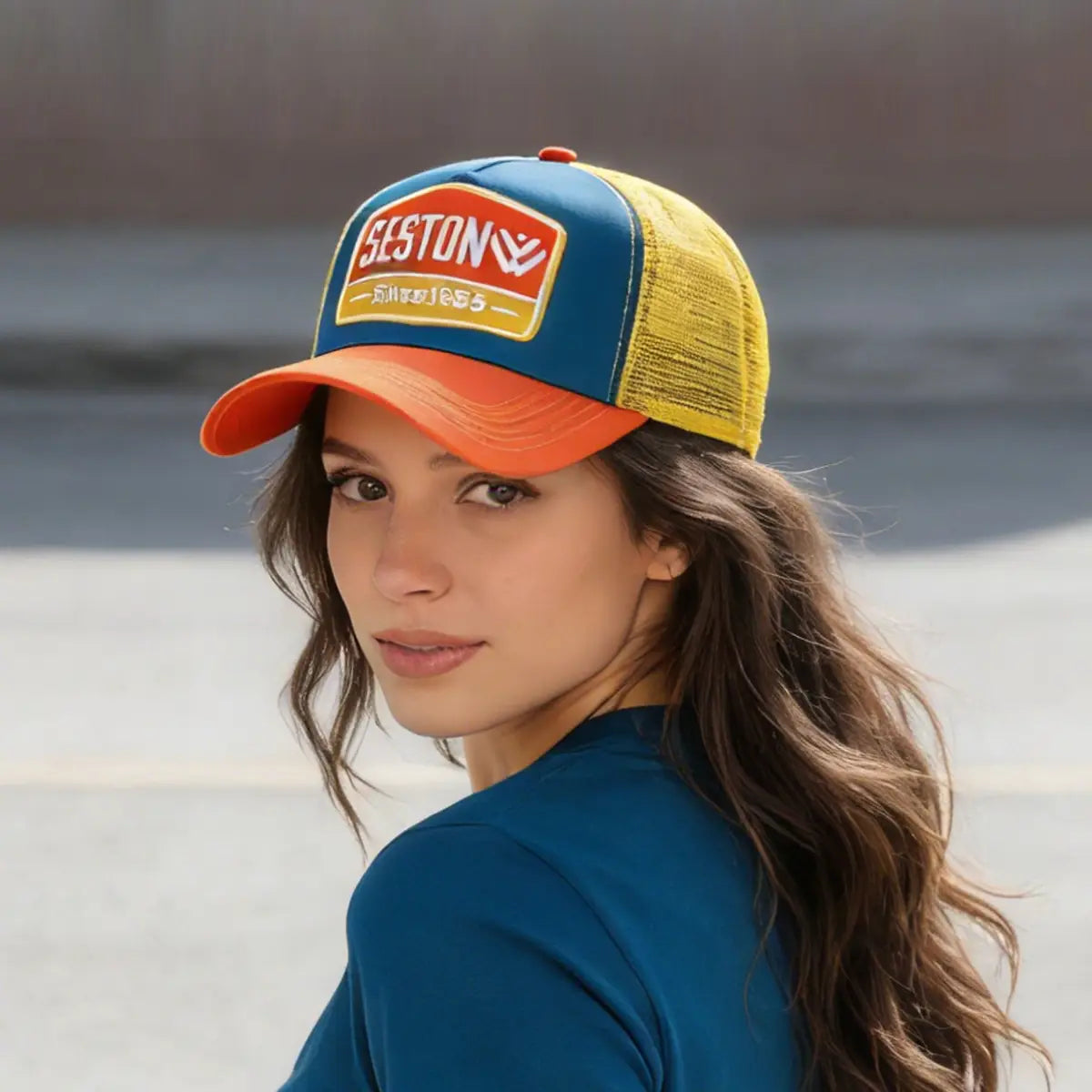 A vibrant trucker hat with a blue front panel orange brim mesh back and yellow accents featuring the Seston logo.