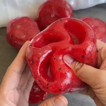 Red translucent dragon fruit-shaped squishy stress relief toy with black seed-like speckles for calming sensory play.