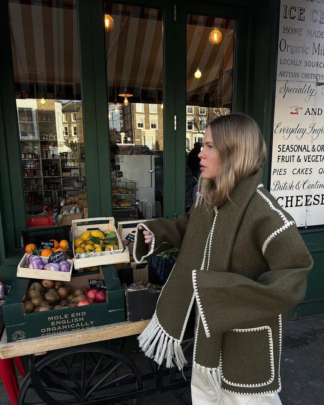 Abrigo oversize de mezcla de lana verde oliva con ribete blanco cosido y detalles de flecos mostrado desde la parte trasera.