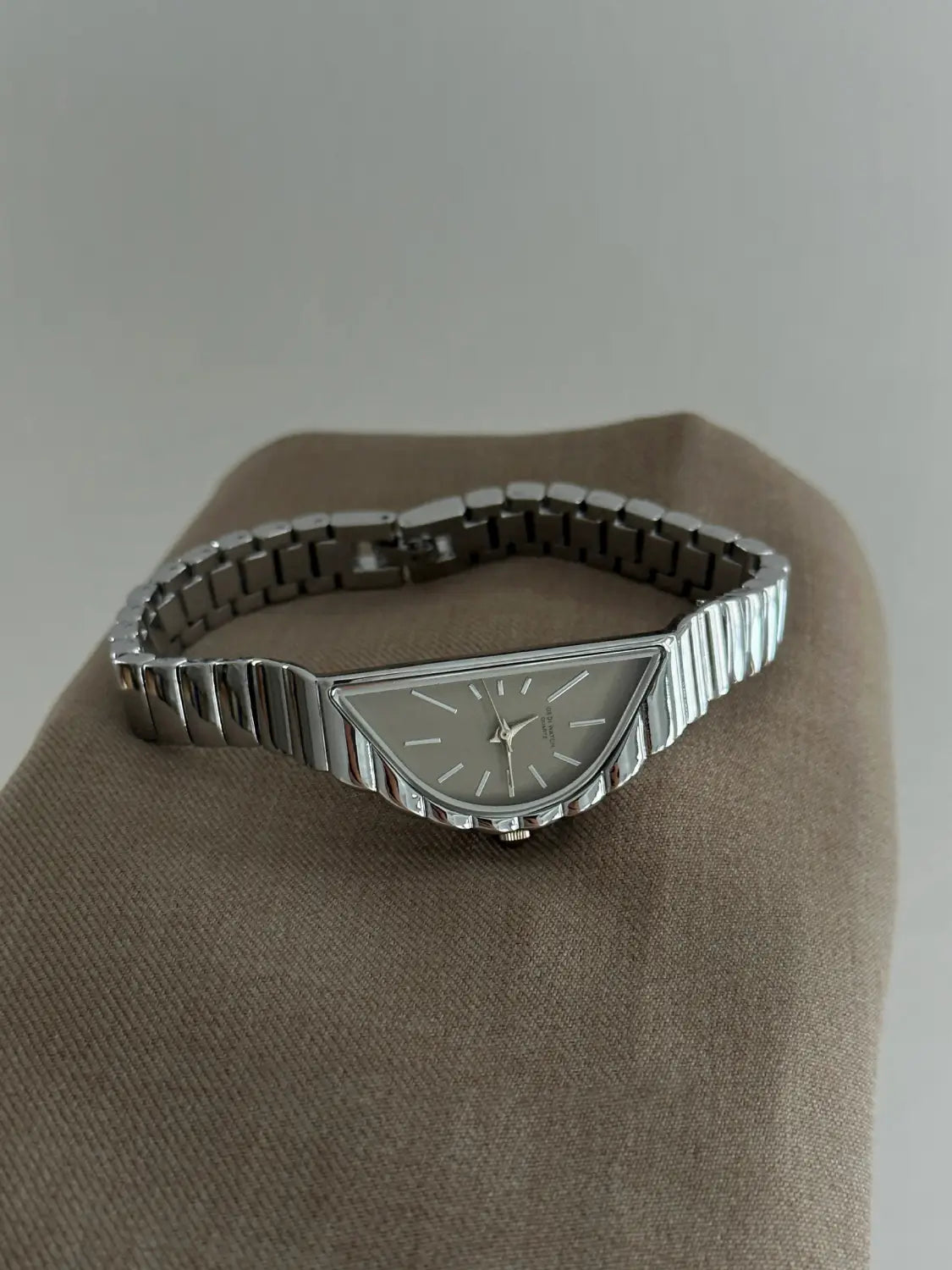 Silver-toned geometric triangle quartz watch with a triangular face, sleek ribbed stainless steel band, and minimalist dial.