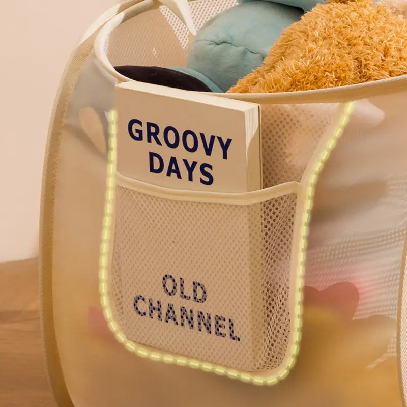 Beige mesh laundry hamper with a front pocket featuring groovy days and old channel text accented by glowing yellow trim used as a large capacity mesh toy storage basket organizer.