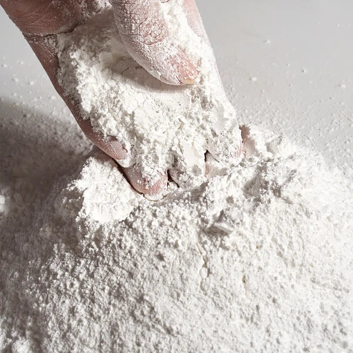 Eine Hand, die in einen Haufen feinen weißen Gipsformguss-Pulvers für DIY-Bastelarbeiten hineindrückt.