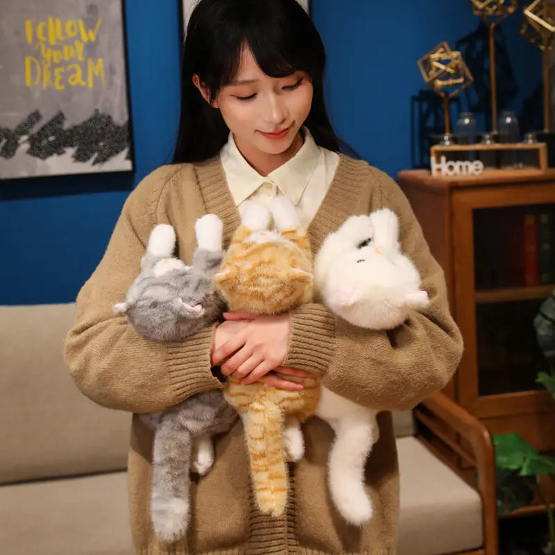 three plush toys featuring soft fur and stitched facial details in gray with white paws and ears orange tabby with black stripes and all-white colors designed as cute kitten stuffed animals and pillows