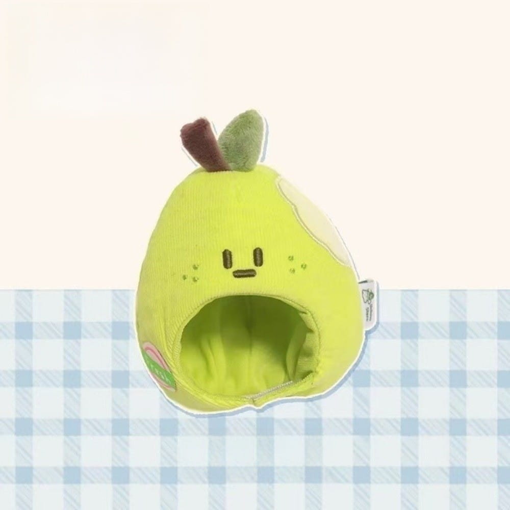 A soft lime-green plush doll headgear shaped like a pear with embroidered facial features and a small leafy stem designed as an animal costume.