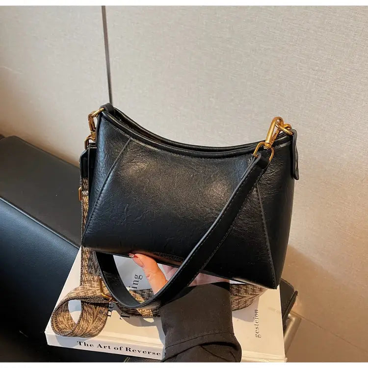 ゴールドトーンの金具と柄のあるストラップを備えた、女性用ブラックレザーのクロスボディショルダーバッグ。