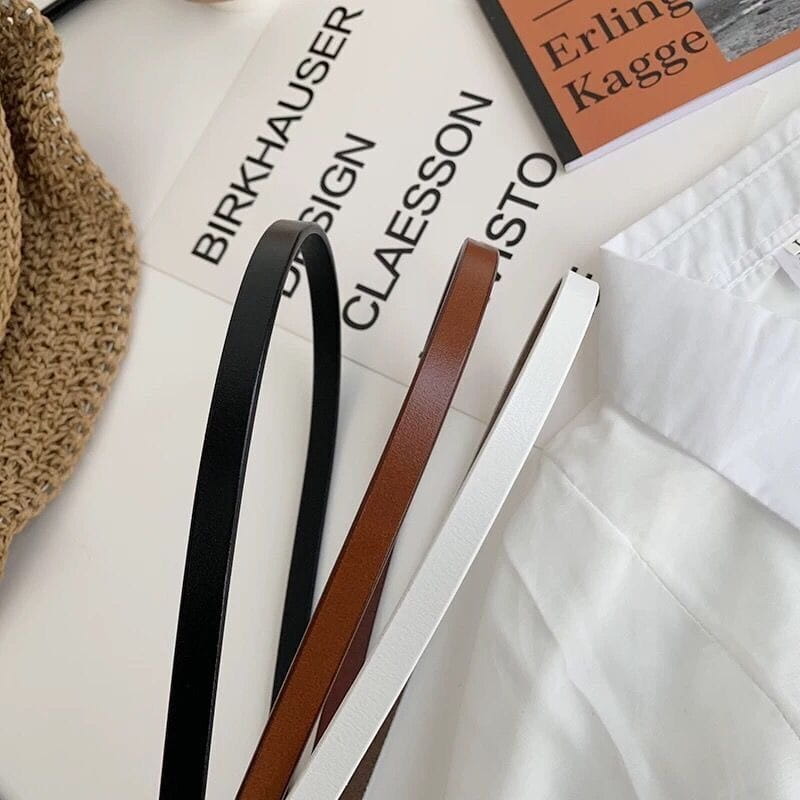 Trois ceintures en cuir PU fines pour femmes, noires, brunes et blanches, avec des boucles dorées, posées à plat sur une surface.