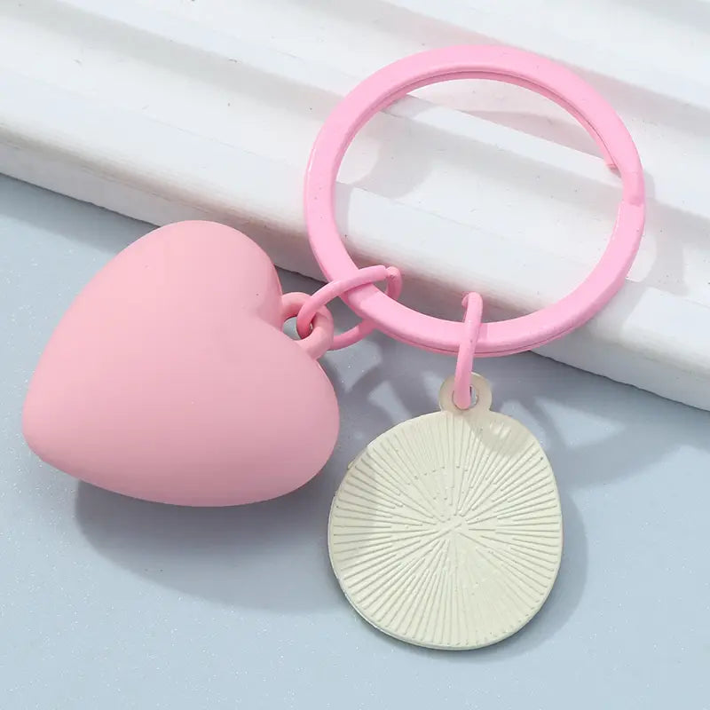 Pink heart smiley face keychain featuring a pink heart-shaped keychain with a matching pink ring and an off-white circular charm with radial grooves.