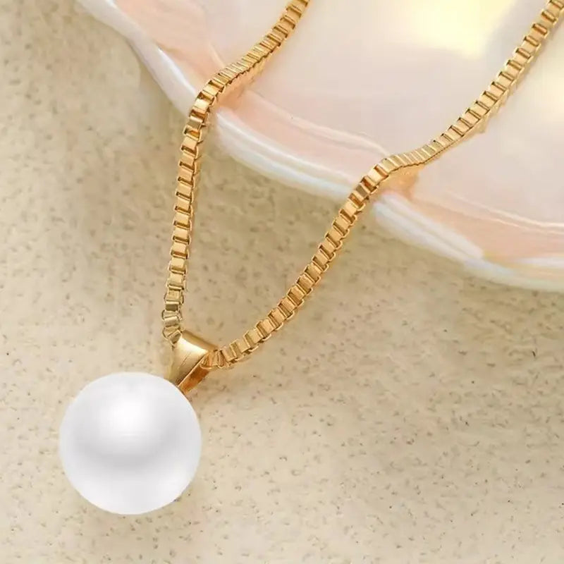 Un collier délicat en chaîne à maillons boîte dorée avec un seul pendentif en perle blanche lustrée, issu d’un ensemble de bijoux à collier à pendentif et boucles d’oreilles.