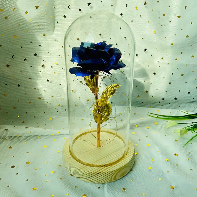 Eine tiefblaue metallische Rose mit goldfoliertem Stiel und Blättern, umschlossen in einer klaren Glaskuppel auf einem hellen Holzsockel, im „Eternal Gold Rose Glass Dome Led Light Gift“.