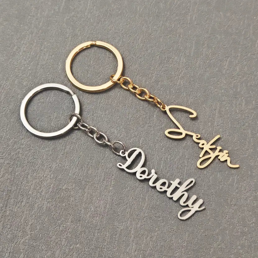 two customized name keychains with delicate cursive engraving one in silver finish with the name dorothy and one in gold finish with the name seafir both attached to metal chains