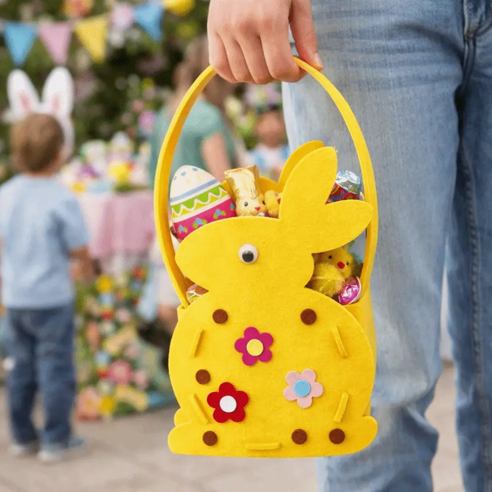 A bright yellow felt Easter bunny basket gift bag adorned with colorful fabric flowers and brown polka dots filled with candy eggs and small chicks.