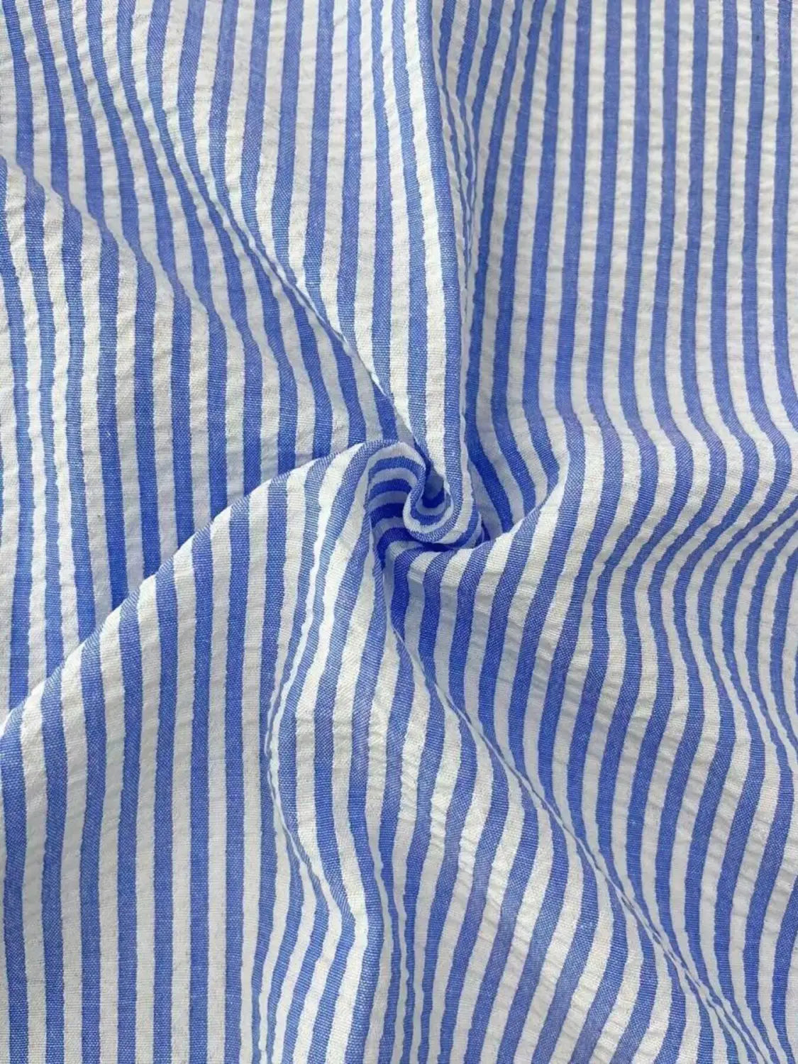 Chemise décontractée boutonnée manches longues à rayures bleues pour homme fabriquée dans un tissu en coton à rayures verticales bleu et blanc, avec une texture froissée discrète.