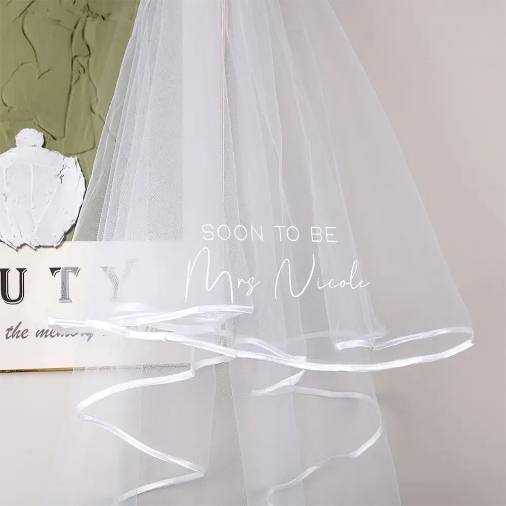 繊細な白いチュール製のパーソナライズされたバチェロレッテパーティー用ベールで、やわらかく流れるようなデザインと控えめなサテンのトリムがあしらわれ、特別なブライダルシャワー用に仕立てられています。