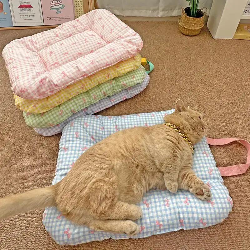 Eine flauschige orangefarbene Katze liegt auf einem hellblauen und weißen Gingham- Karomuster-Bogenkissen für Haustiere, das aus Baumwolle besteht und rosafarbene Schleifenmotive sowie einen passenden rosafarbenen Riemen aufweist.