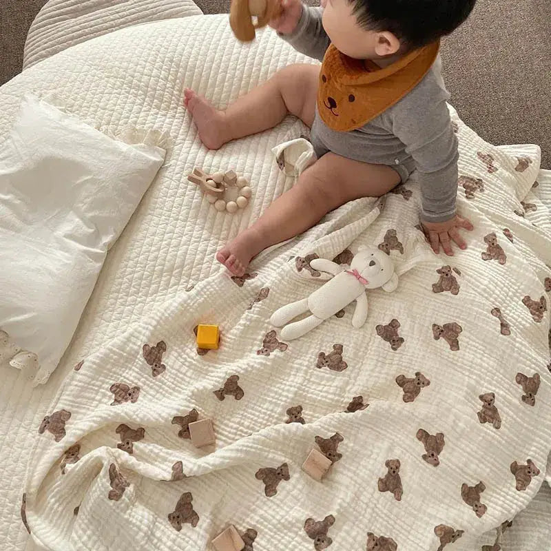 ein weiches Baby-Badehandtuch und eine Wickeldecke aus Muslin in sanftem Off-White mit dezentem, gepolstertem Relief und verstreuten Designs brauner Teddybären