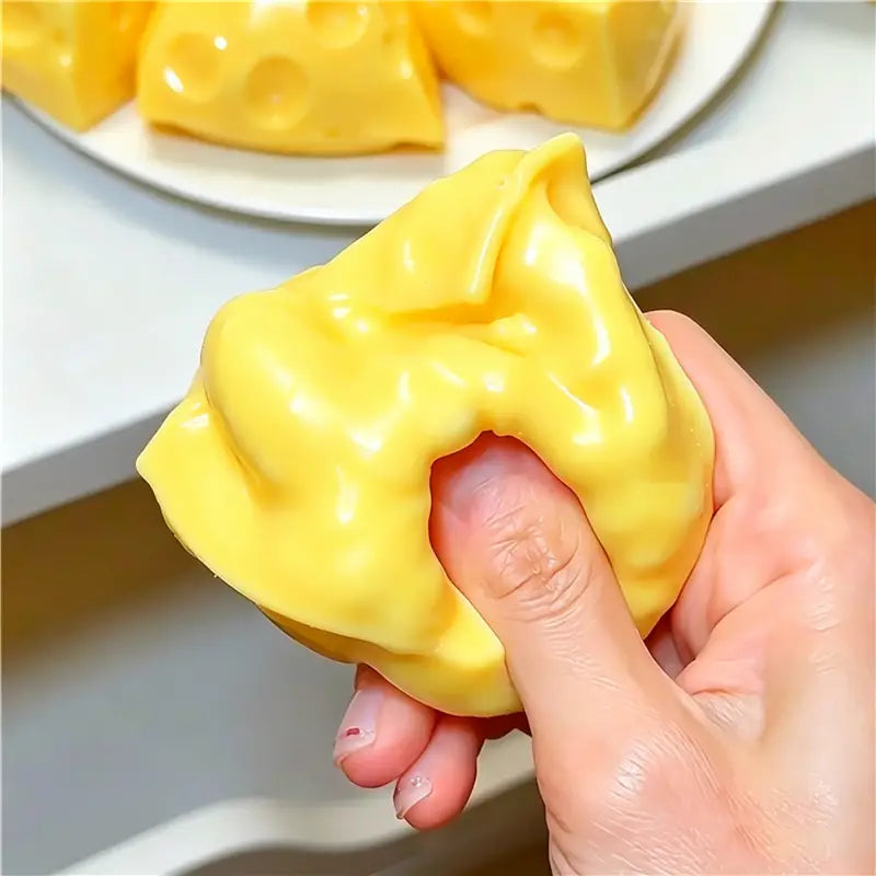 Un jouet sensoriel de type balle anti-stress en forme d’arachide jaune, en forme de fromage, souple et déformable, comprimé dans une main.