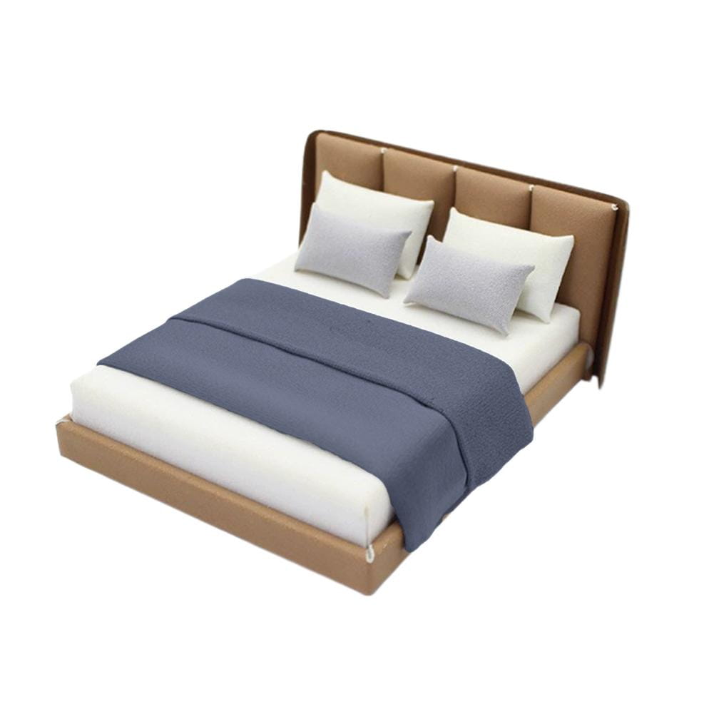 Miniature dollhouse double bed with brown upholstered frame, white mattress, gray pillows, and navy blue textured blanket in cream style.