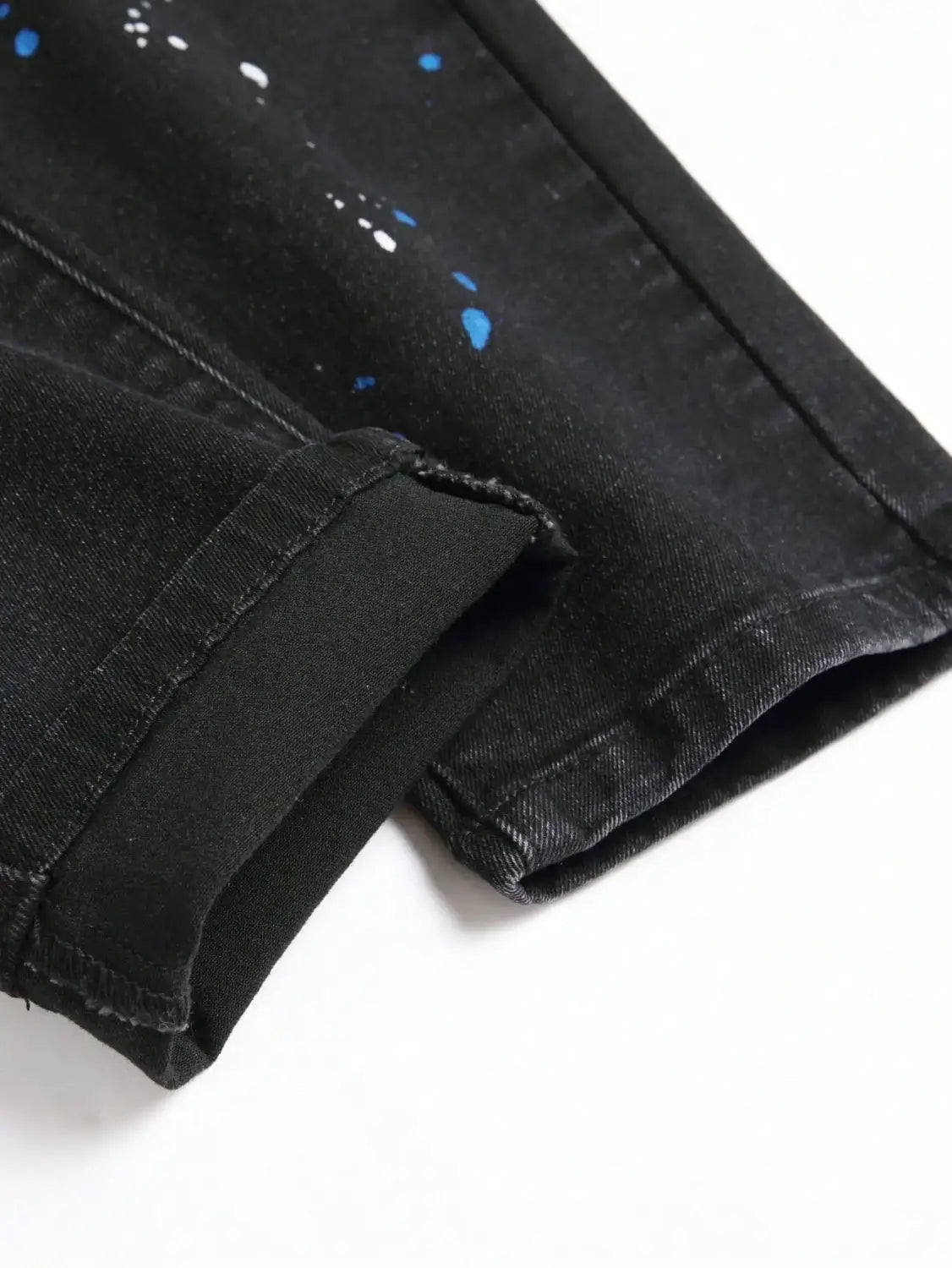 Jeans denim skinny extensibles déchirés Y2K pour hommes en noir, avec un motif d’éclaboussures de peinture bleu et blanc.