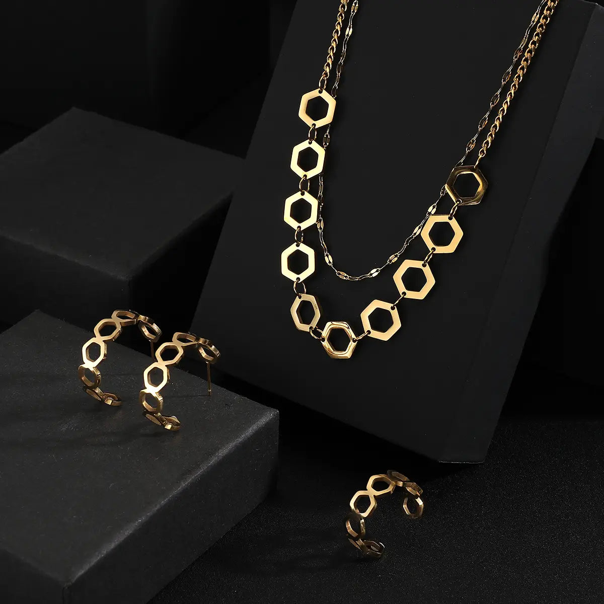 Juego de joyería de acero inoxidable color dorado para mujeres, con un collar con cadena hexagonal de tono dorado, diseño en capas y eslabones geométricos alternados sólidos y abiertos.