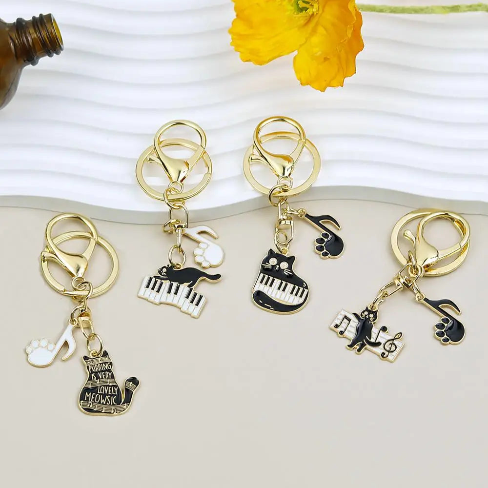 gold-toned keychains featuring black and white enamel cat designs with piano keys musical notes and paw prints for black cat piano keychain music lover gift