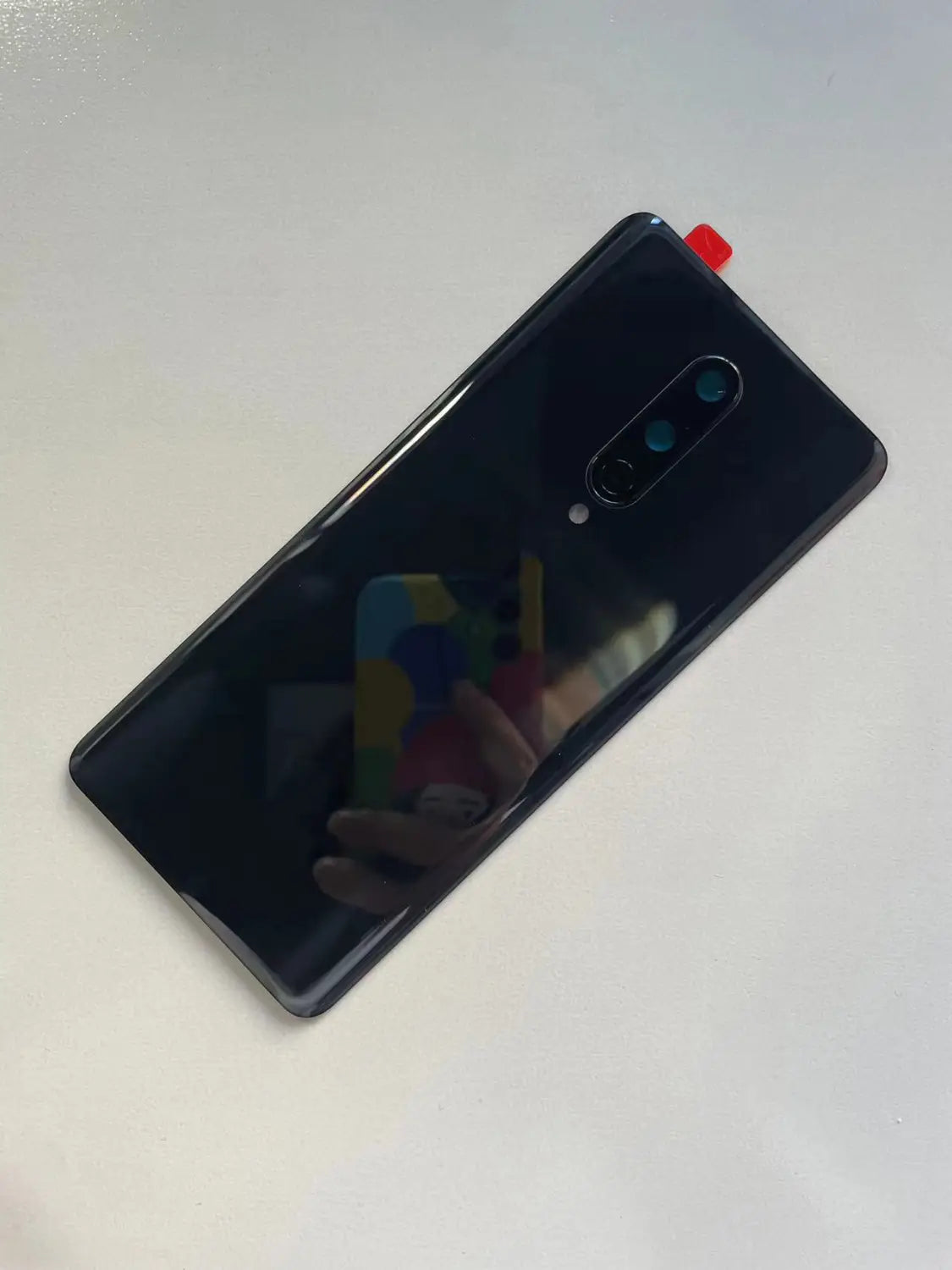 schwarze, glänzende Akkufachabdeckung aus hochwertigem Gorilla-Glas als Rückseitenverkleidung für Oneplus 8 mit Triple-Kamera-Setup und kleiner roter Lasche in der oberen Ecke