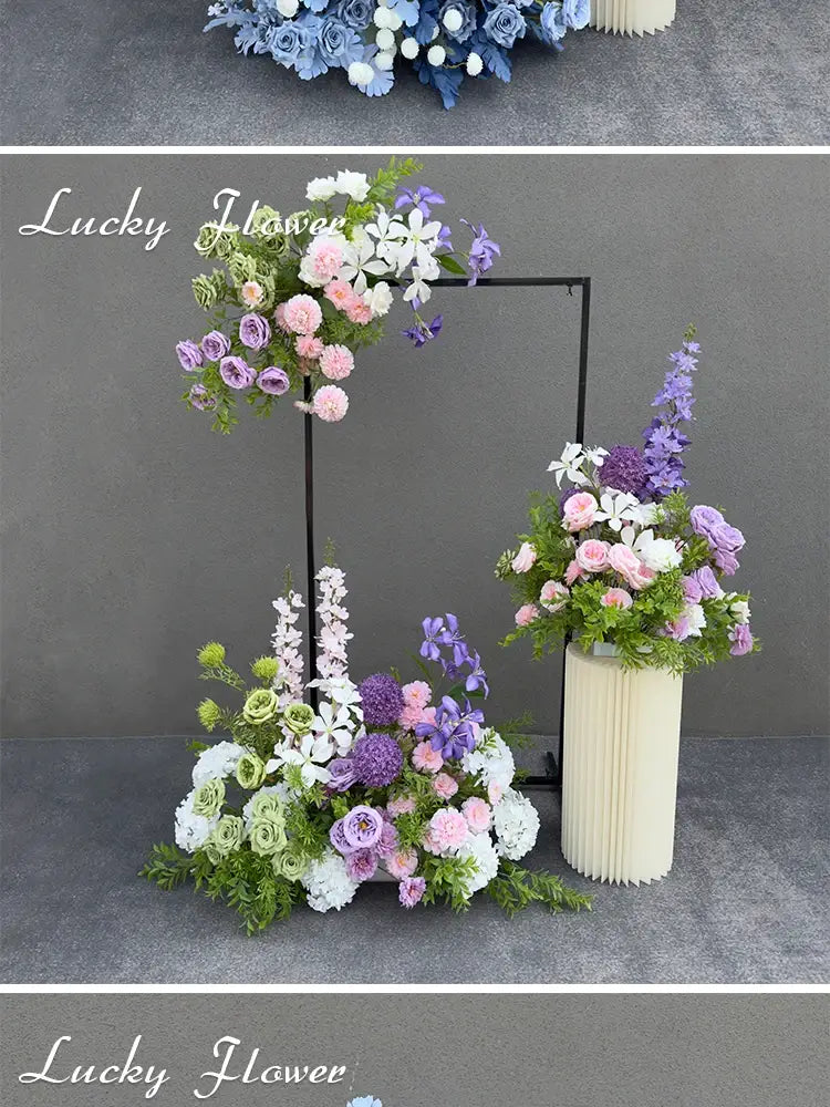 A tall cream-colored pleated vase holding a lush arrangement of purple pink and white artificial flowers for a wedding arch floral backdrop.