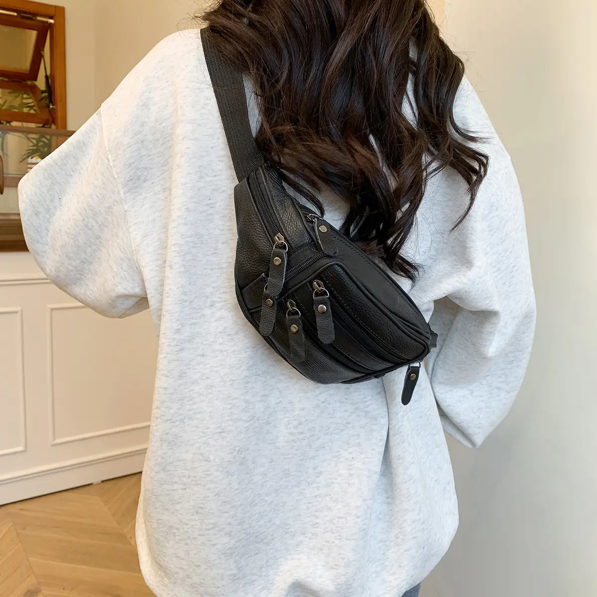 Schwarze Gürteltasche aus echtem Leder mit mehreren Reißverschlüssen und silberfarbenen Beschlägen, entworfen als Crossbody-Bauchtasche.