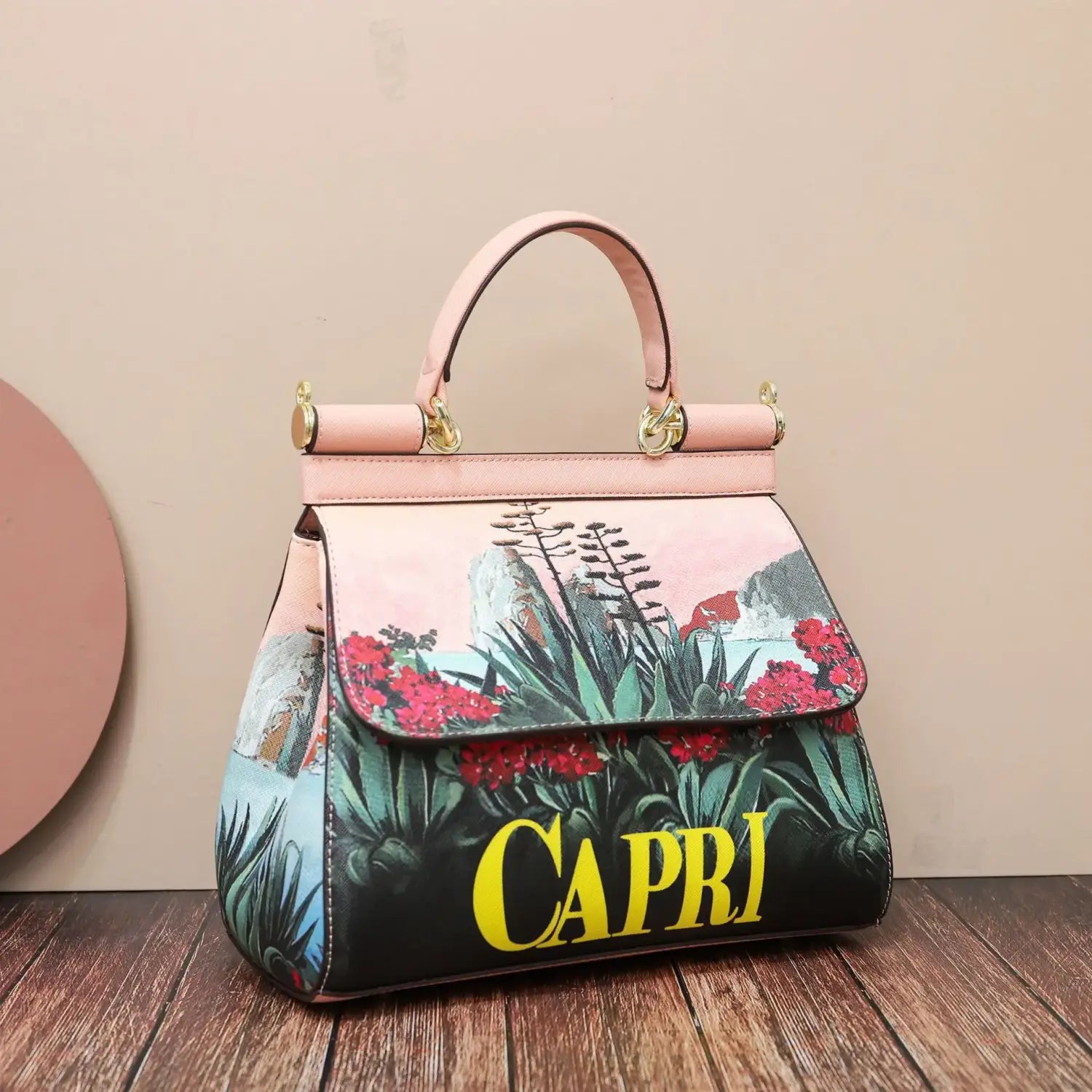 Sac bandoulière en cuir vintage, art raffiné, en cuir rose, avec un imprimé floral et paysager vibrant comprenant des fleurs rouges, un feuillage vert et le mot « Capri » en lettres jaunes audacieuses.